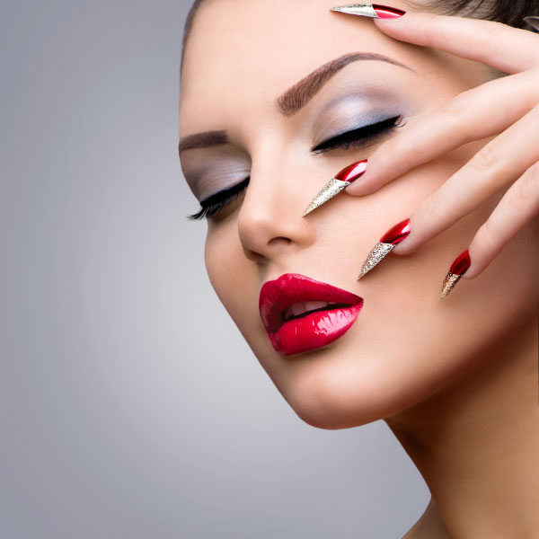 Professional beauty makeup with bold red lips, eyelash extensions, flawless skin, elegant nail art, and perfectly shaped eyebrows.